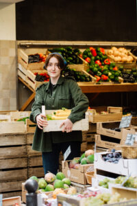 une jeune femme porte une cagette remplie de légumes dans une boutique de centre ville